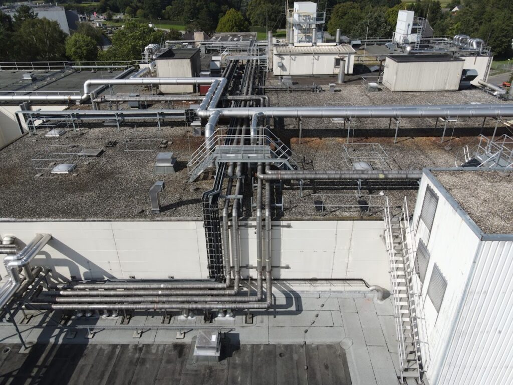 Blick von oben auf das Dach einer Industrieanlage mit einem komplexen Netzwerk aus isolierten und blanken Rohrleitungen, die in einer Ammoniak-Kälteanlage installiert sind.