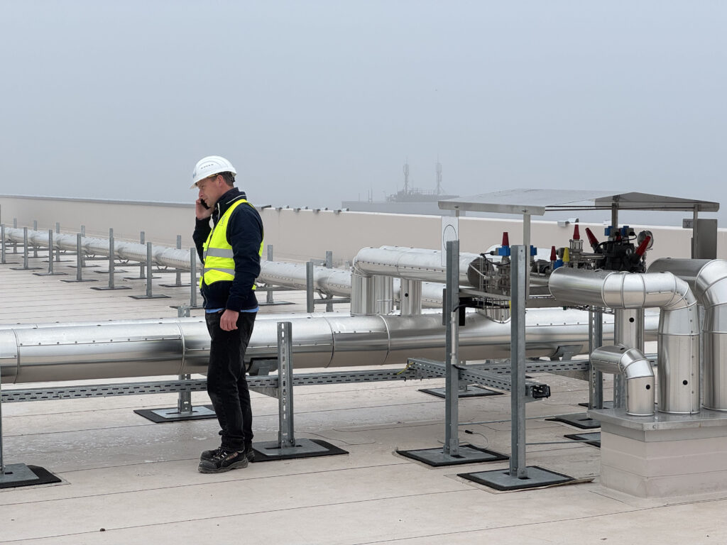 Ein Techniker im Gespräch auf dem Dach, umgeben von neuen Rohrleitungen für die Integration eines Spiralfrosters in eine bestehende NH₃-Tiefkühlanlage.